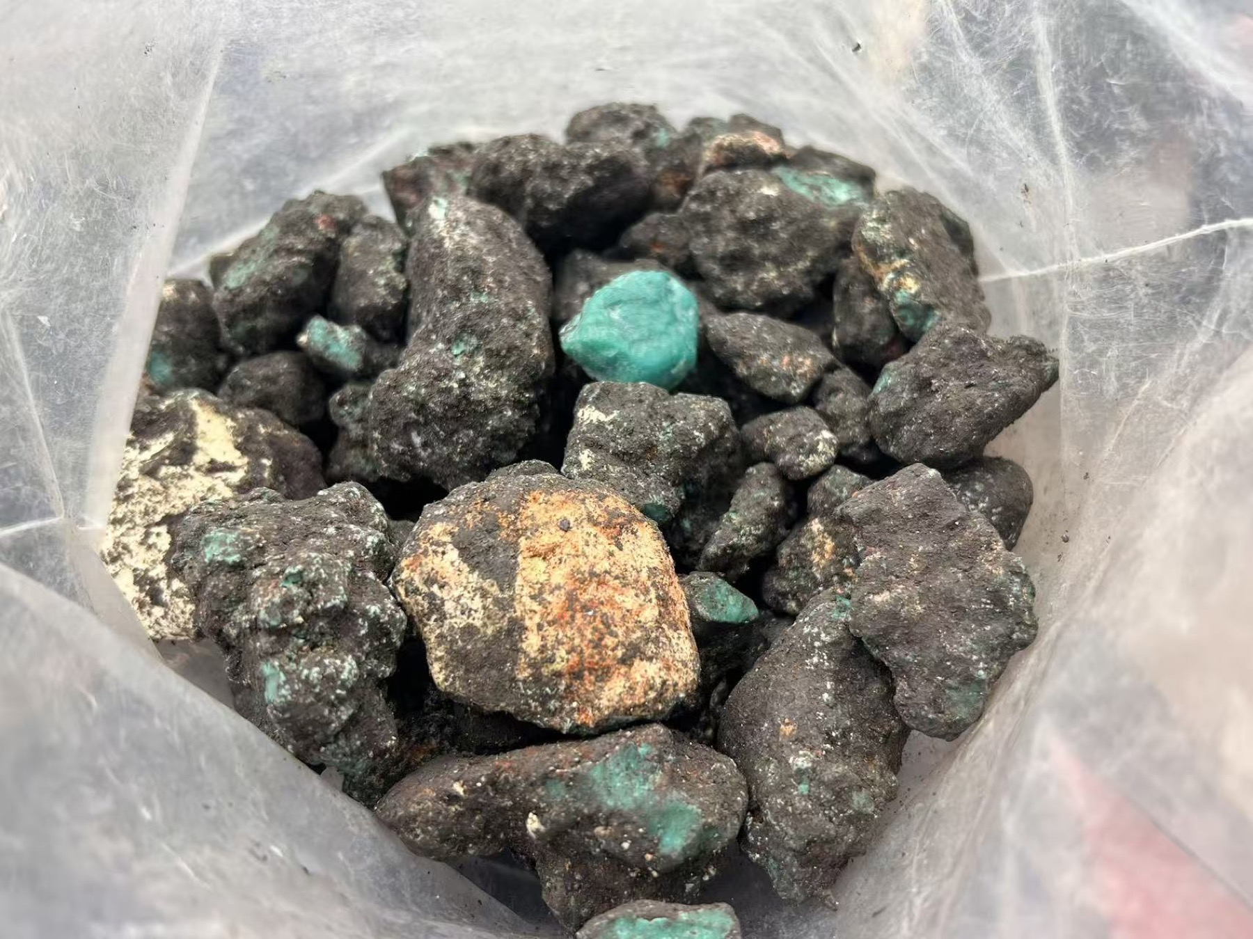 Dark host-rock rough with small areas of turquoise visible